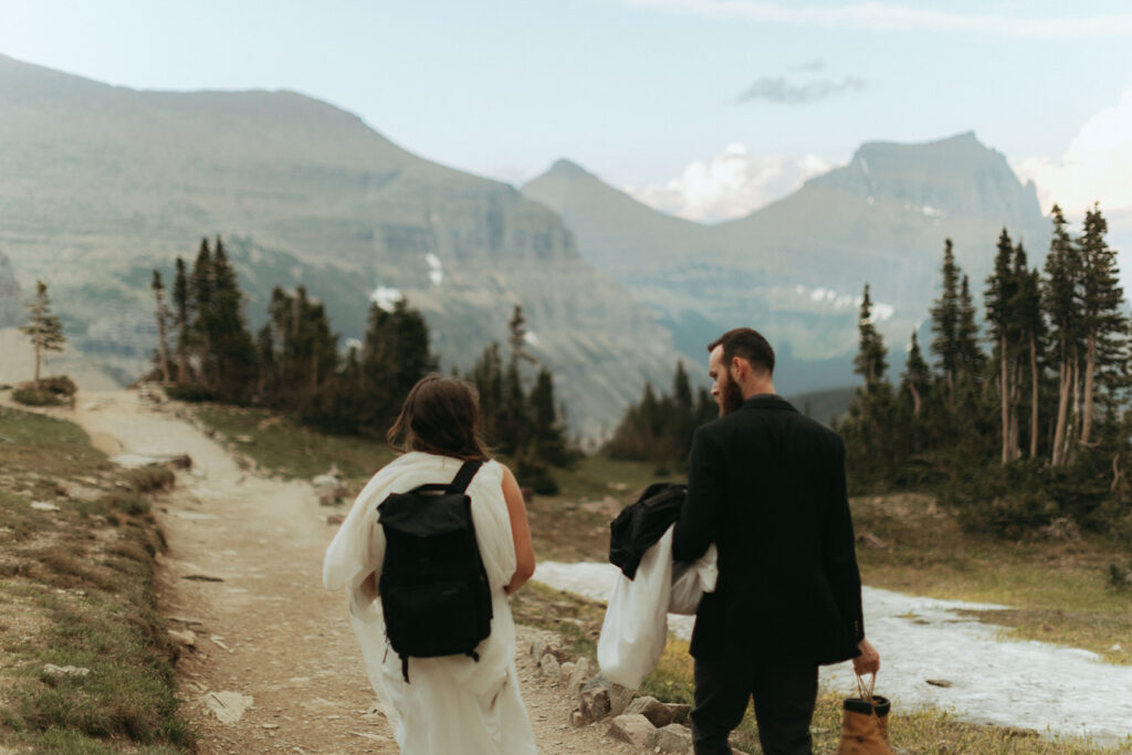 groom carries clothes walking with bride on path at outdoor adventure elopement