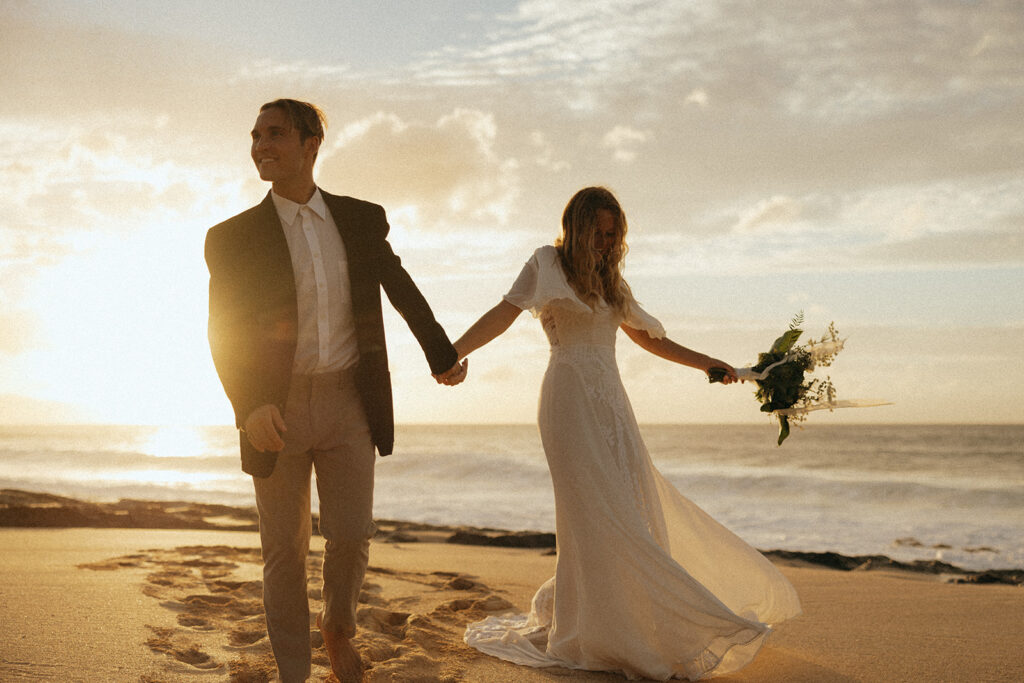 couple walks holding hands at sunrise on beach at Hawaii photography content day
