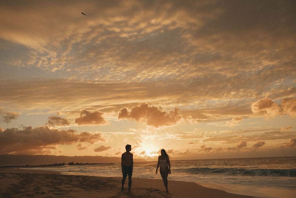 couple walks through beach at sunset during Hawaii photography content day