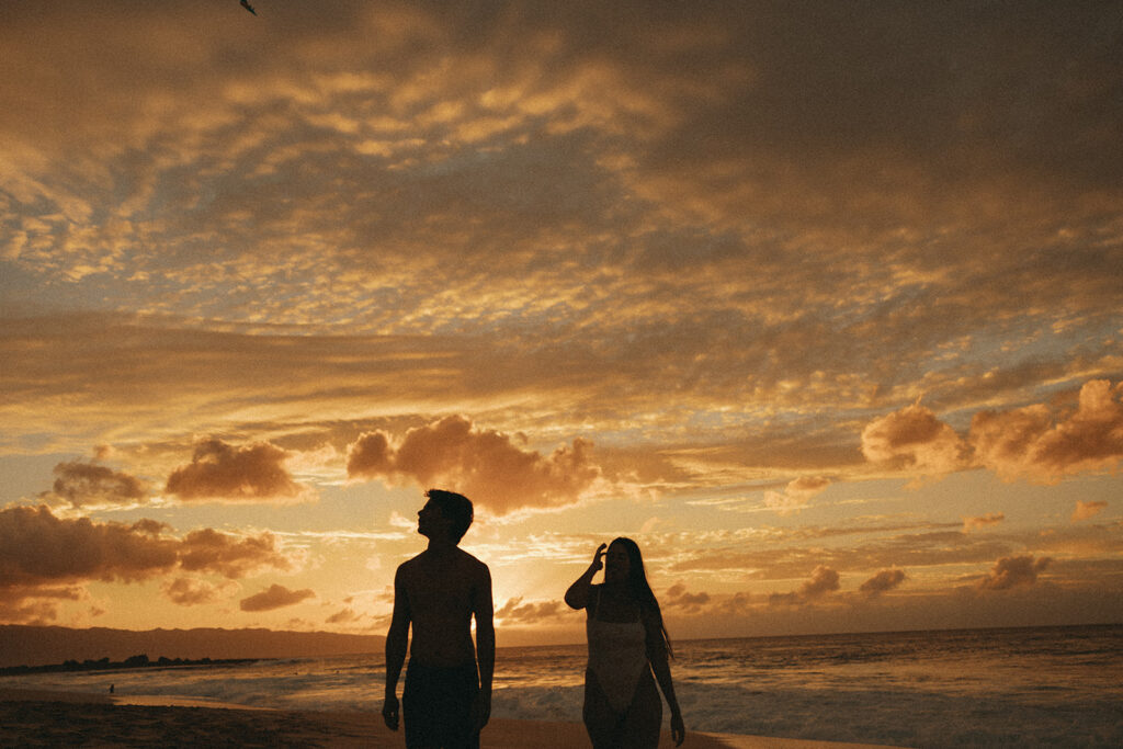 couple walks through beach at sunset during Hawaii photography content day