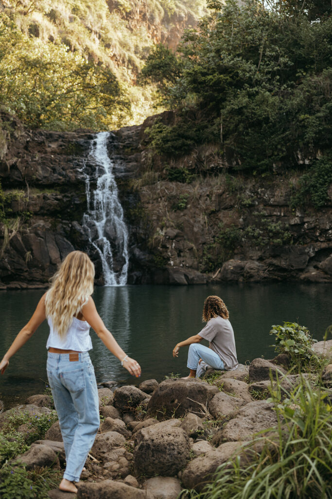 couple walks and sits beside Hawaii waterfall