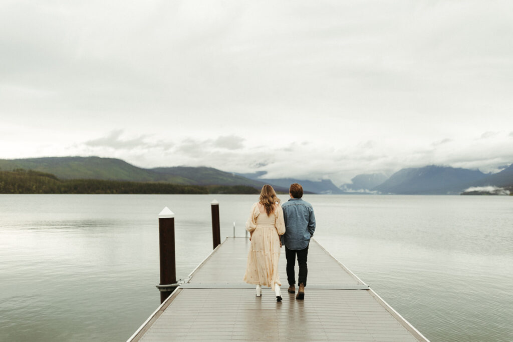 couple walks along pier at glacier national park lake 