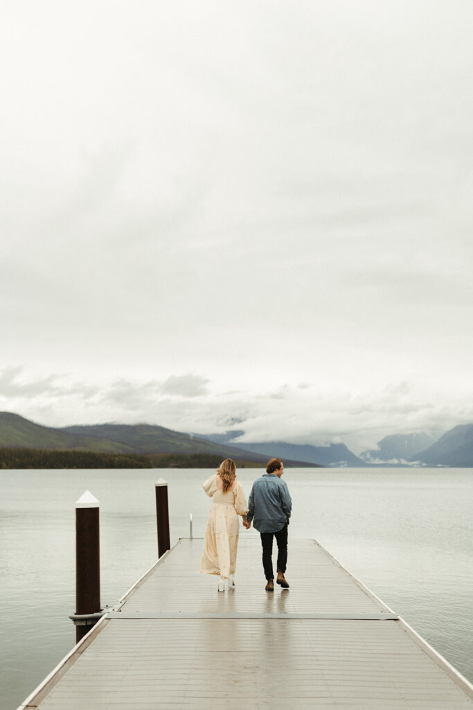 couple walks along pier using adventure ideas at Glacier National Park engagement session