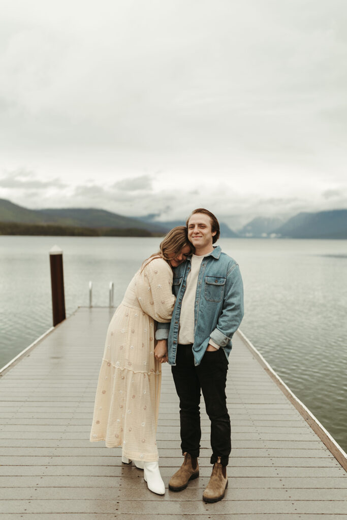 couple embraces on pier at lake in  Glacier National Park 
