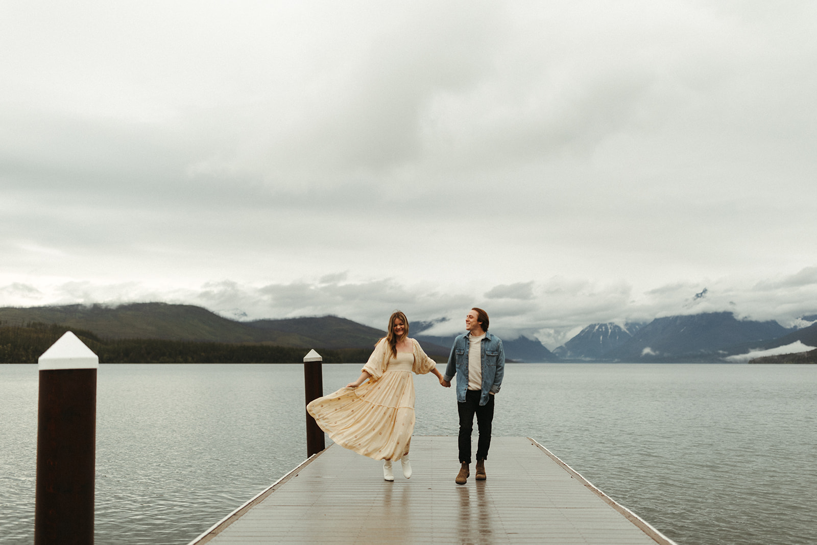 couple walks along pier on lake at Glacier National Park engagement