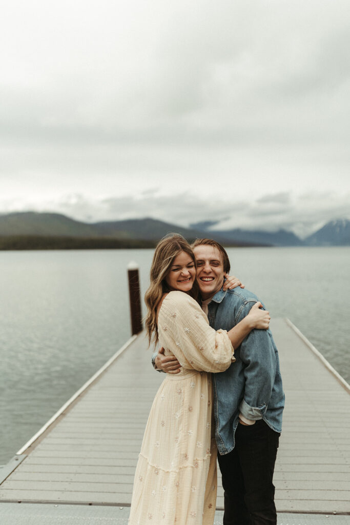 couple embraces on pier on lake at Glacier National Park engagement session