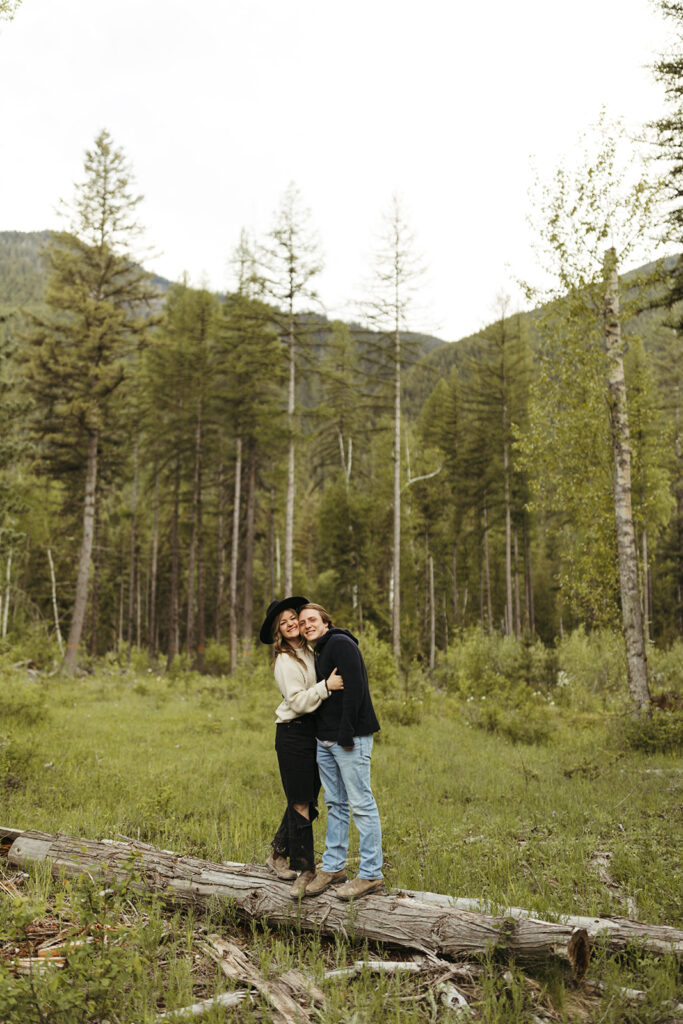 couple hugs standing on fallen log at Glacier National Park engagement session