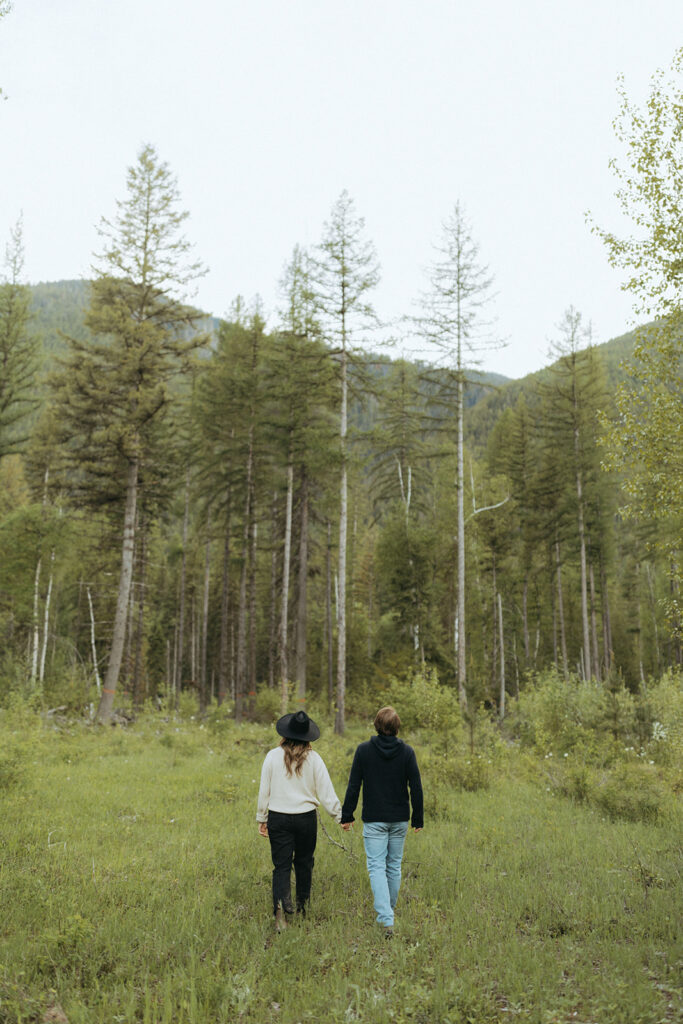 couple walks through woods using adventure ideas at Glacier National Park engagement session