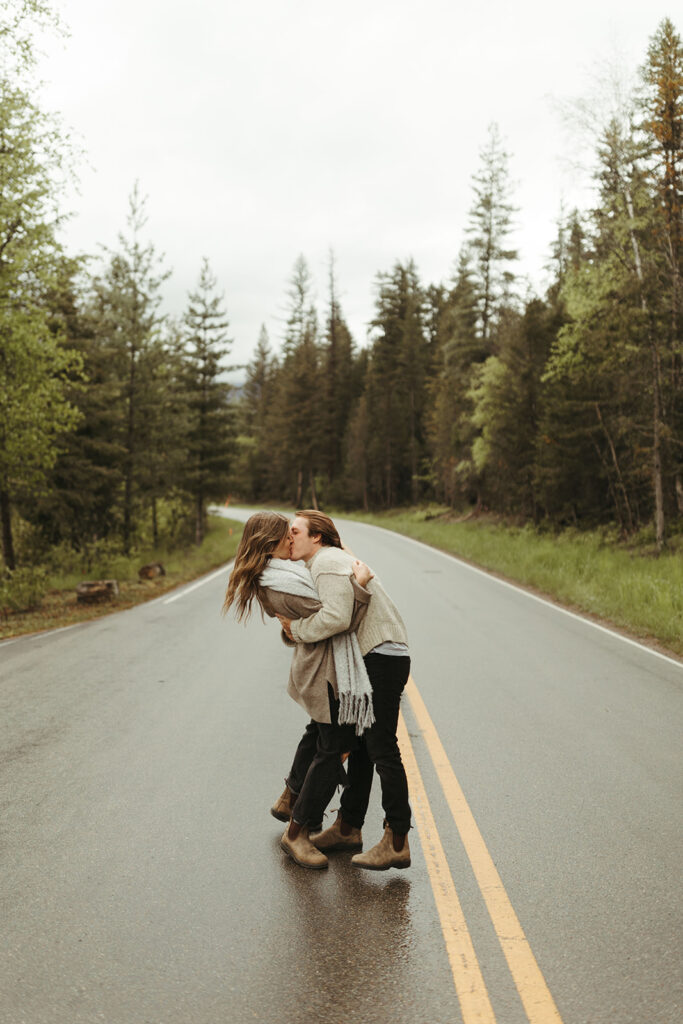 couple gets adventure ideas while kissing on road at Glacier National Park engagement session