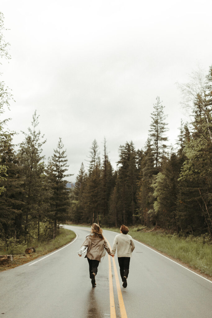 couple runs along wooded road using adventure ideas at Glacier National Park engagement session
