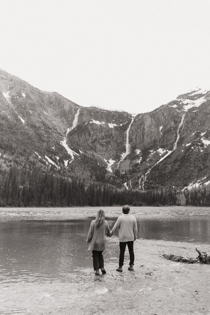couple uses adventure ideas standing beside lake at Glacier National Park engagement session