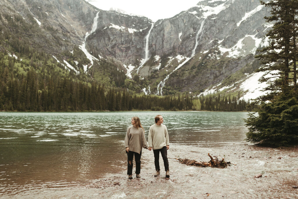couple holds hands in front of lake at glacier national park