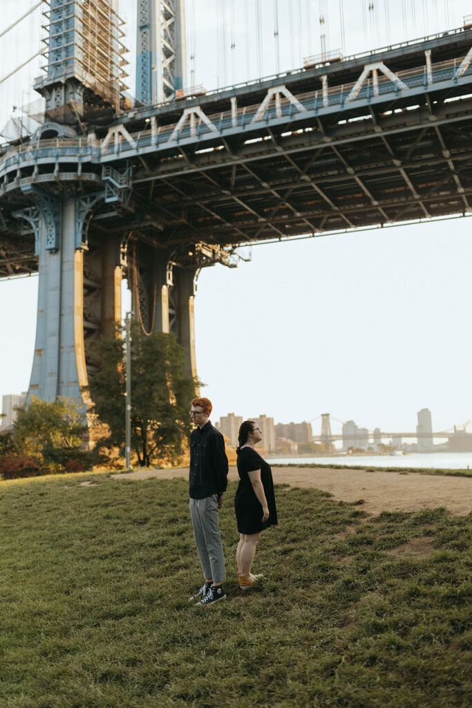 couple stands back to back under manhattan bridge as marriage proposal ideas