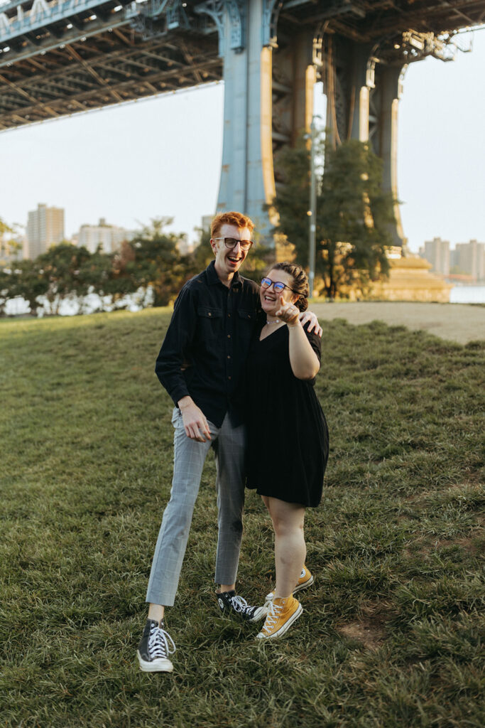 couple laughs after marriage proposal under Manhattan bridge