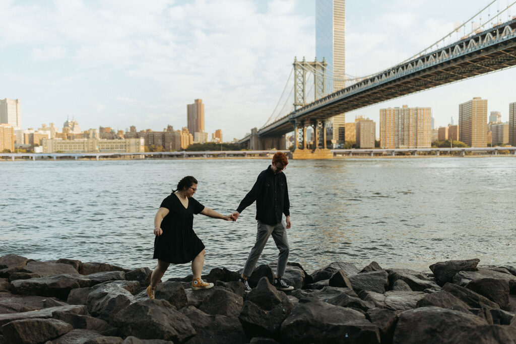 couple walks across rocks by brooklyn waterside for marriage proposal ideas