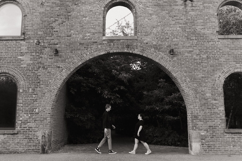 couple walk towards each other under brick bridge 