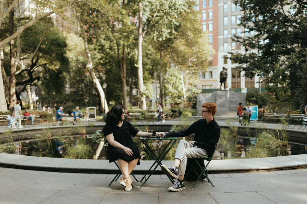 couple holds hands seated at table in Central park