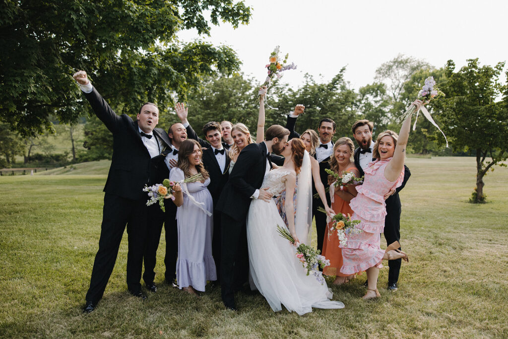 couple kisses surrounded by wedding party cheering at garden party wedding