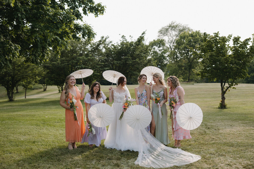 bride holds umbrellas with bridesmaids at garden party wedding