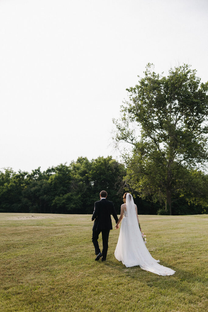 couple walks through field holding hands at garden party wedding