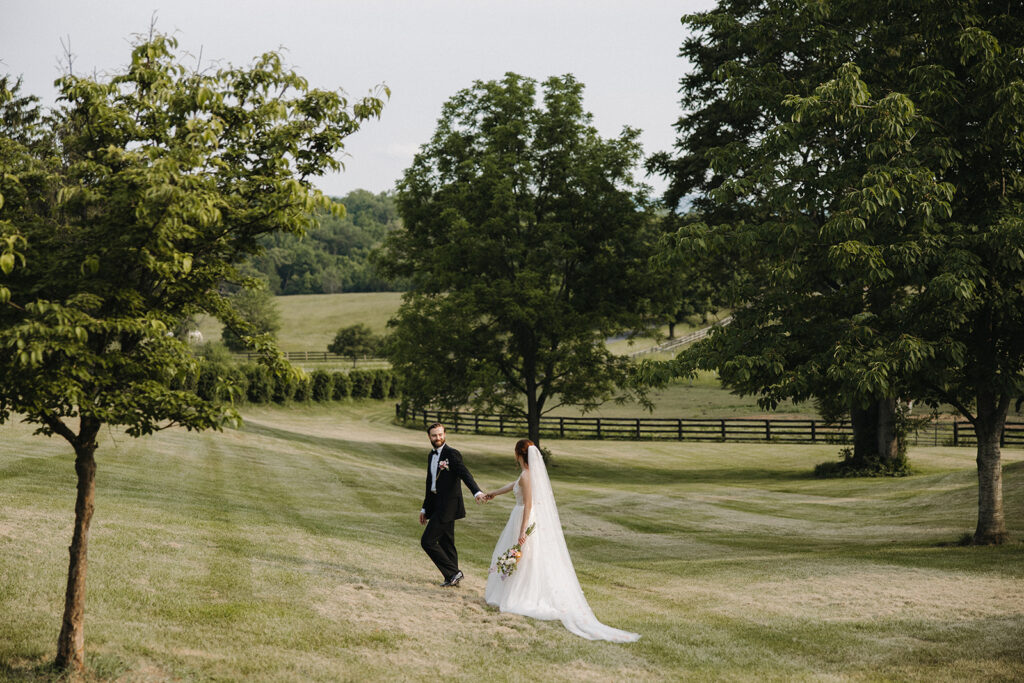 couple walks through field holding hands at garden party wedding