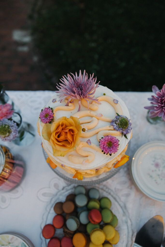 colorful flower wedding cake on table with with colorful macarons 