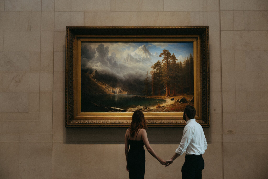 couple holds hands in front of painting at art gallery engagement session