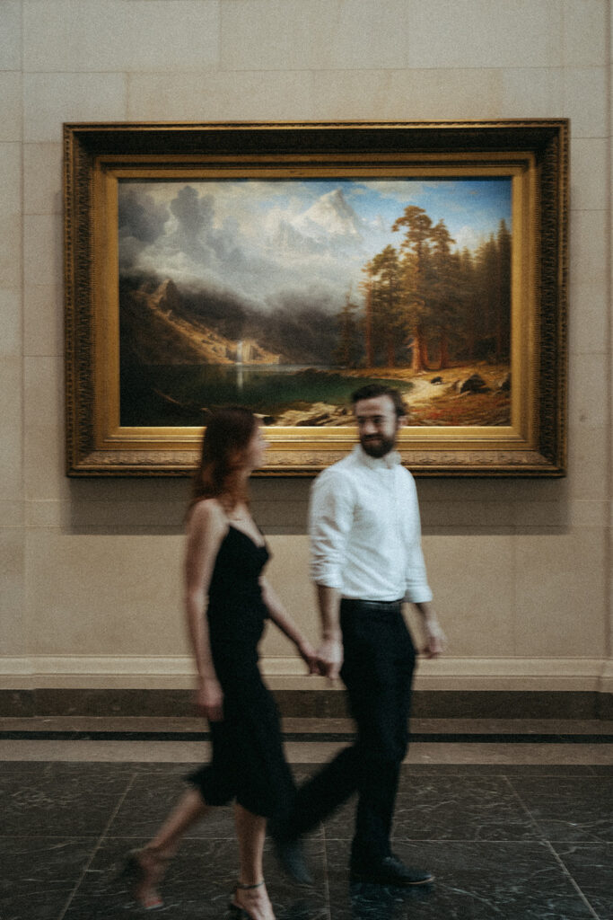 couple walks holding hands at art gallery engagement session