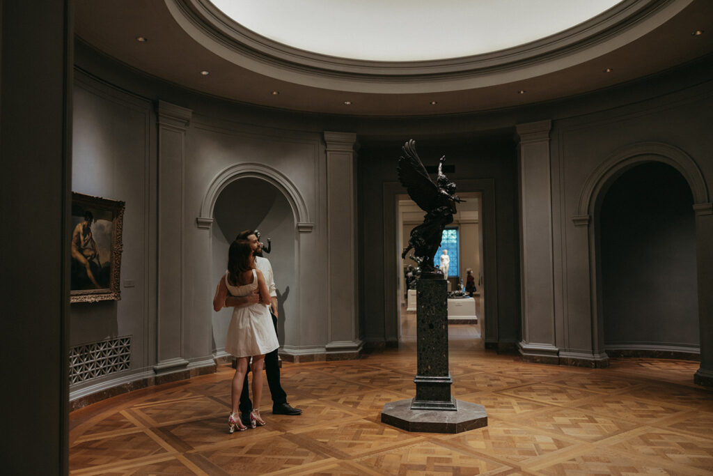couple embraces by sculpture at art gallery engagement session