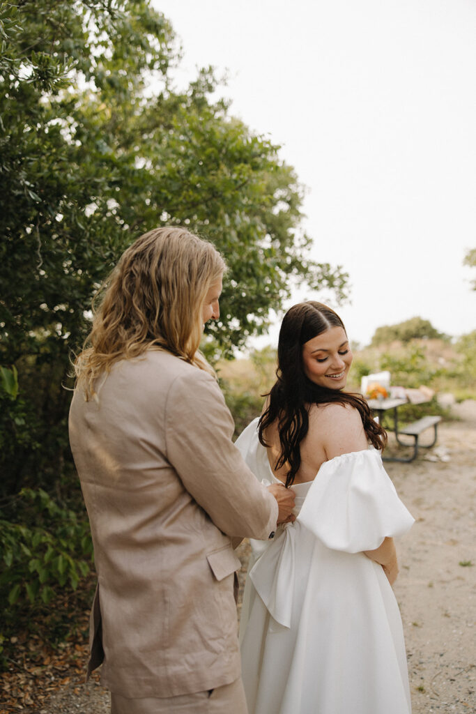 groom helps bride get ready at Virginia Beach elopement