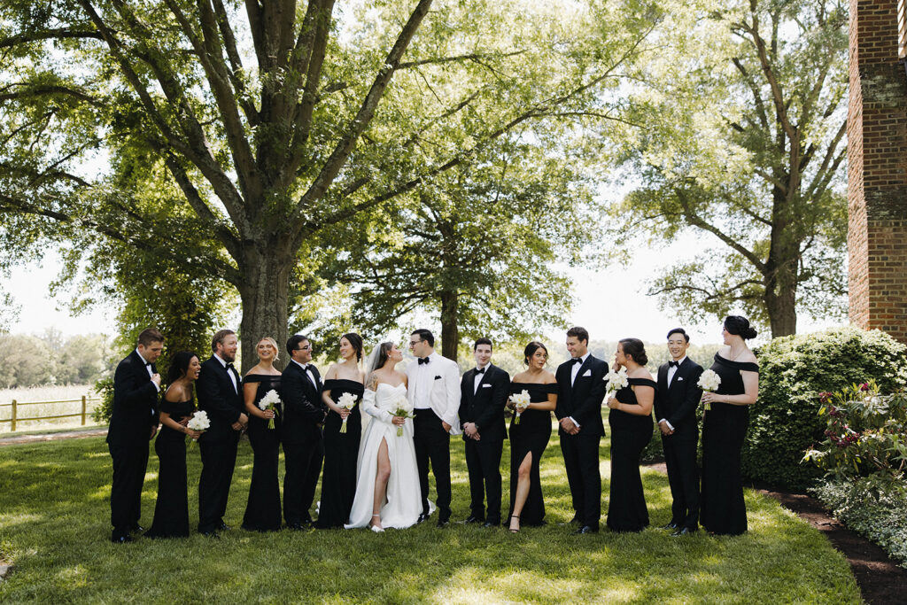 couple poses with wedding party at outdoor wedding