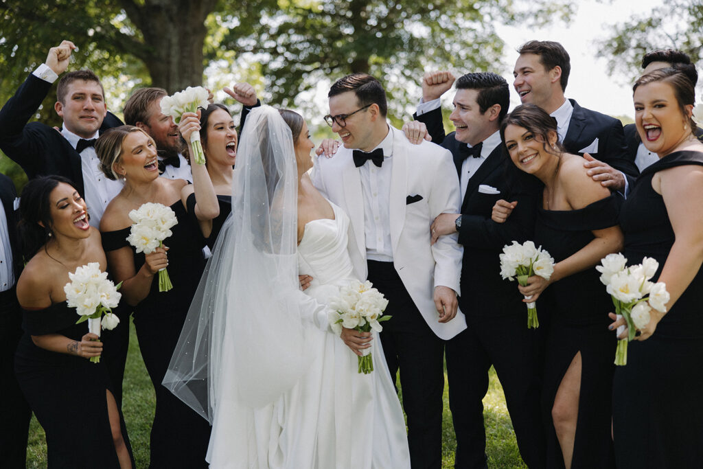 couple laughs with wedding party at outdoor wedding
