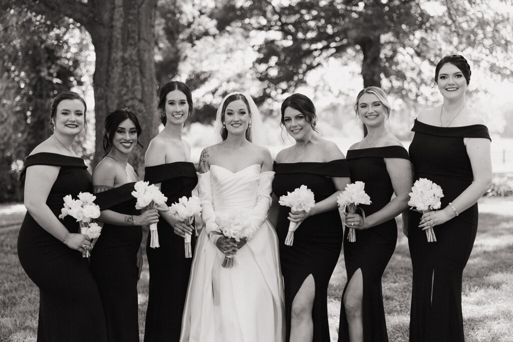 couple holds white wedding bouquets with bridesmaids