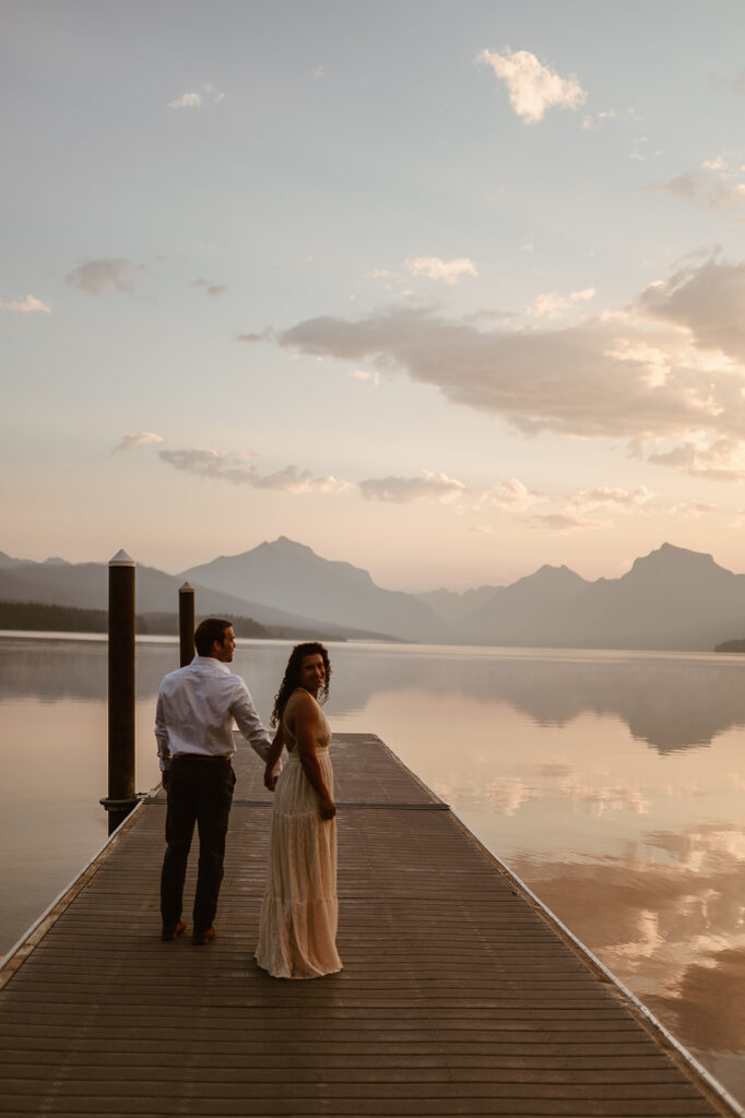 couple holds hands on pier at sunrise lake engagement