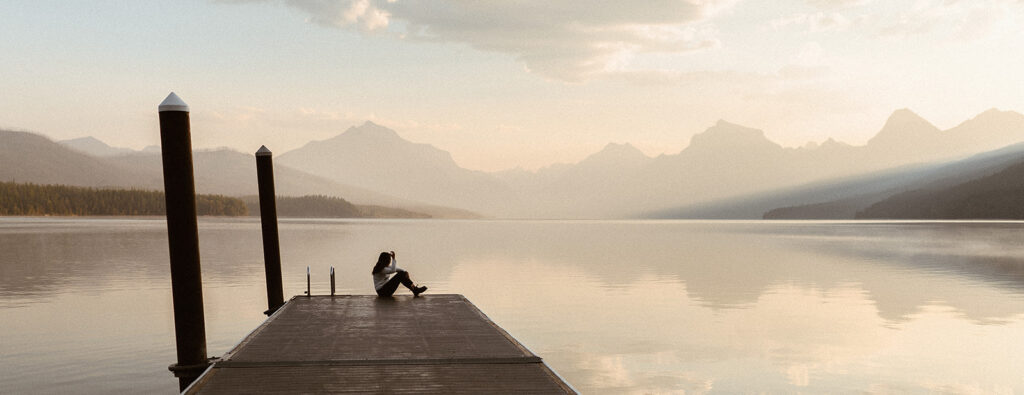 photographer sits on pier by lake at sunrise