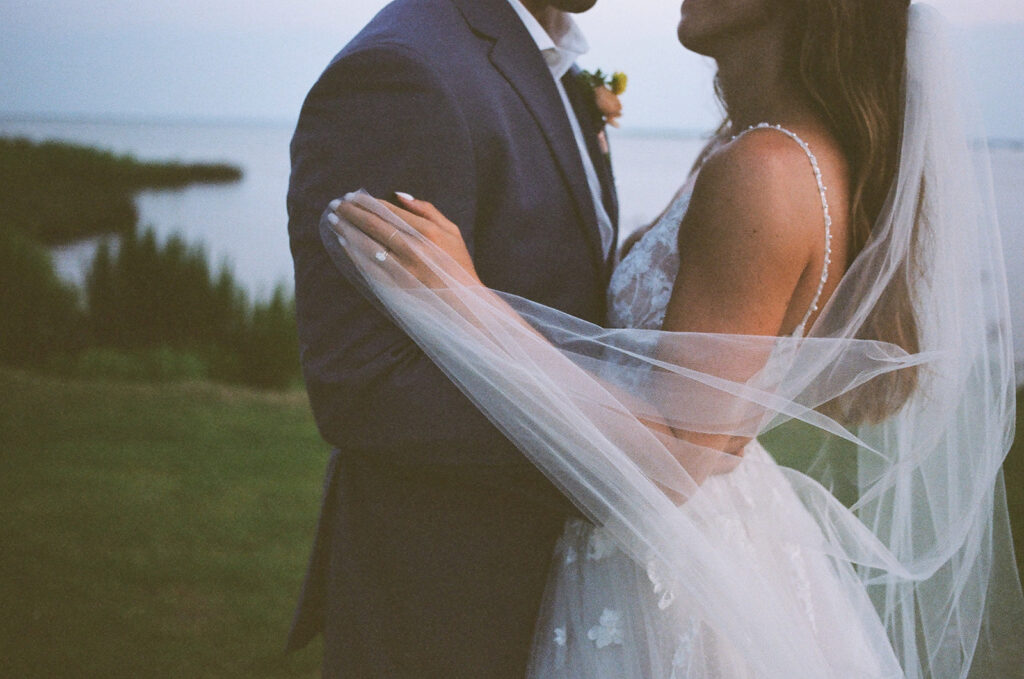 couple embraces under wedding veil before wedding reception in backyard
