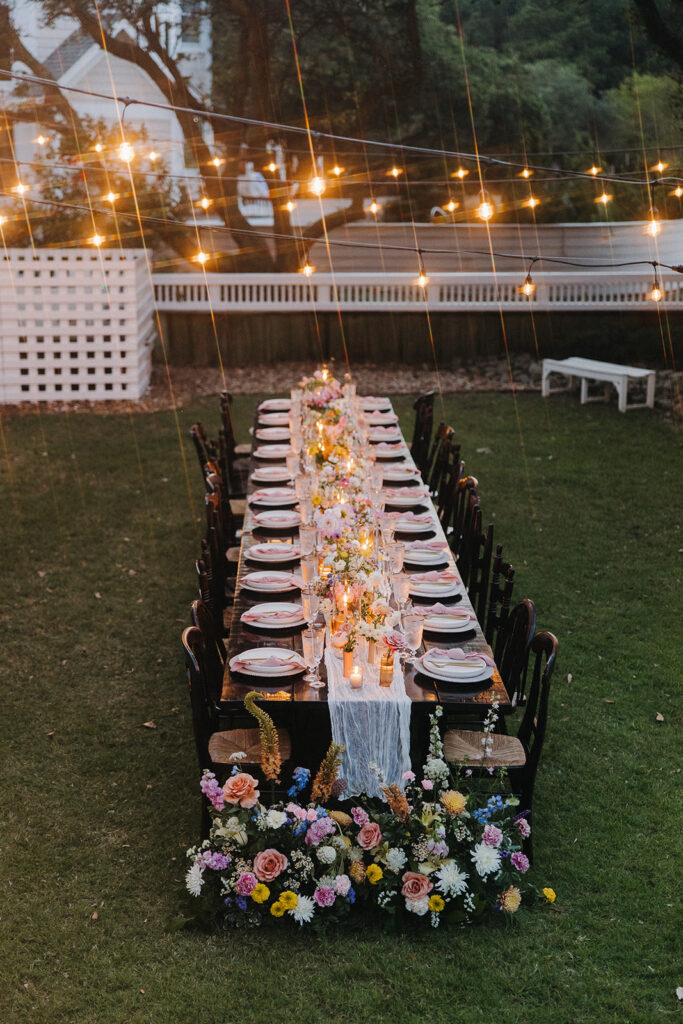floral decor on long table under twinkle lights at wedding reception in backyard