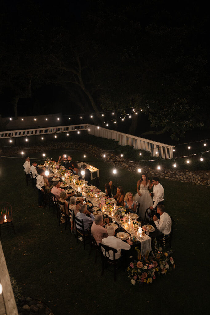floral decor on long table under twinkle lights at wedding reception in backyard