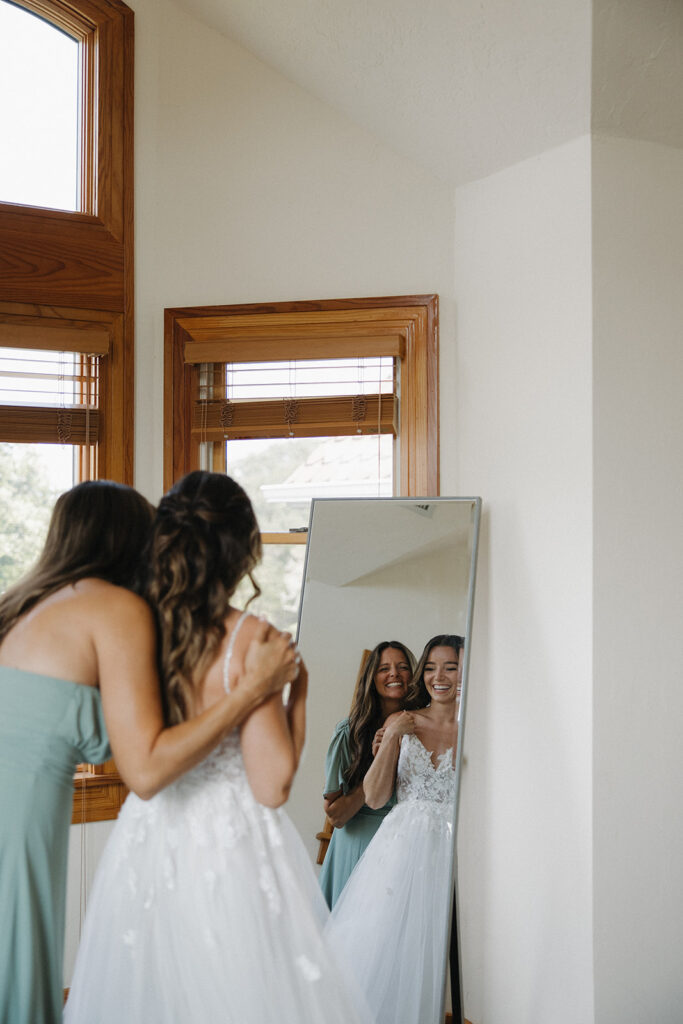 bride gets ready with bridesmaid looking into mirror