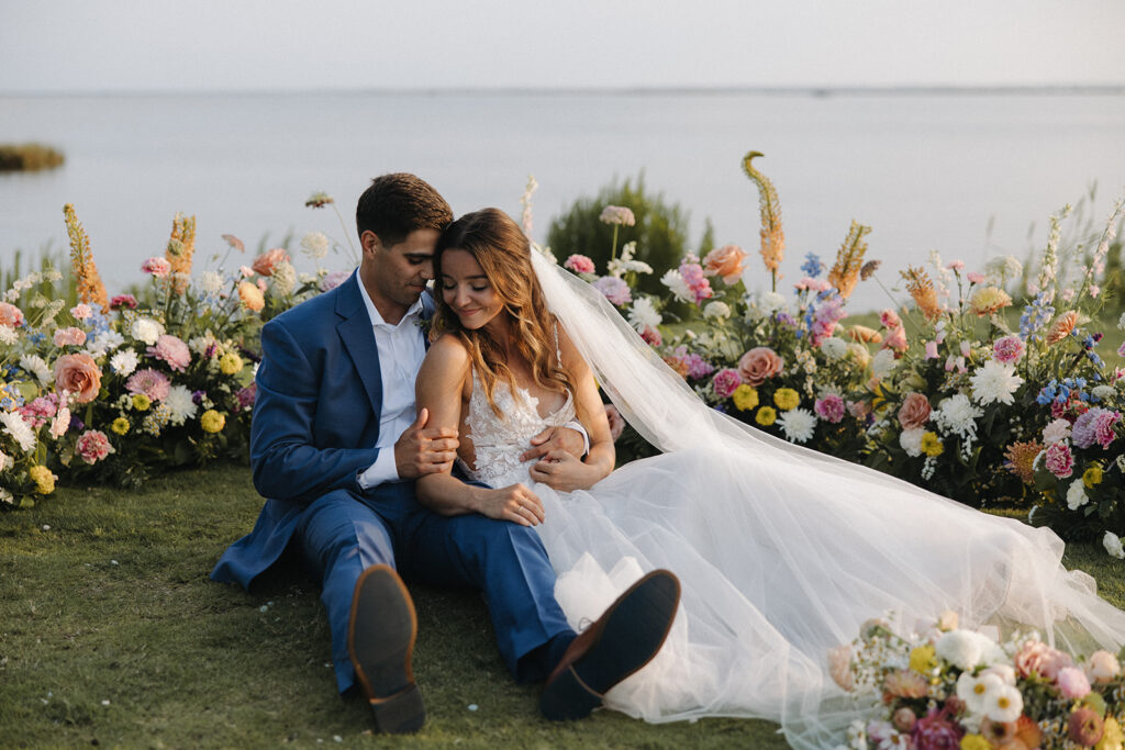 couple sits beside wedding flowers at outdoor wedding
