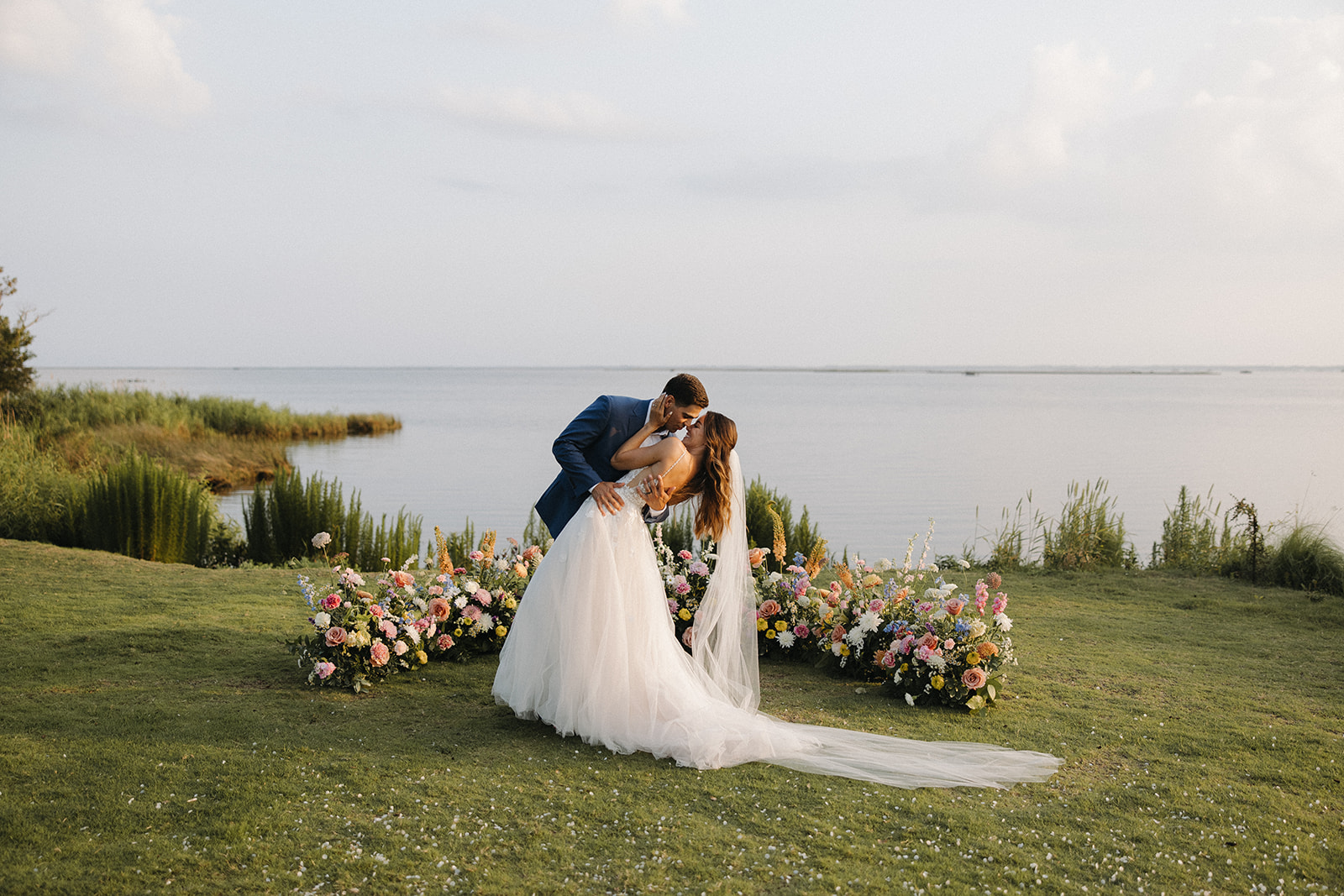 couple kisses at waterfront beside wedding flowers