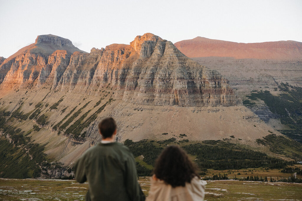 couple holds hands looking at sunset mountain