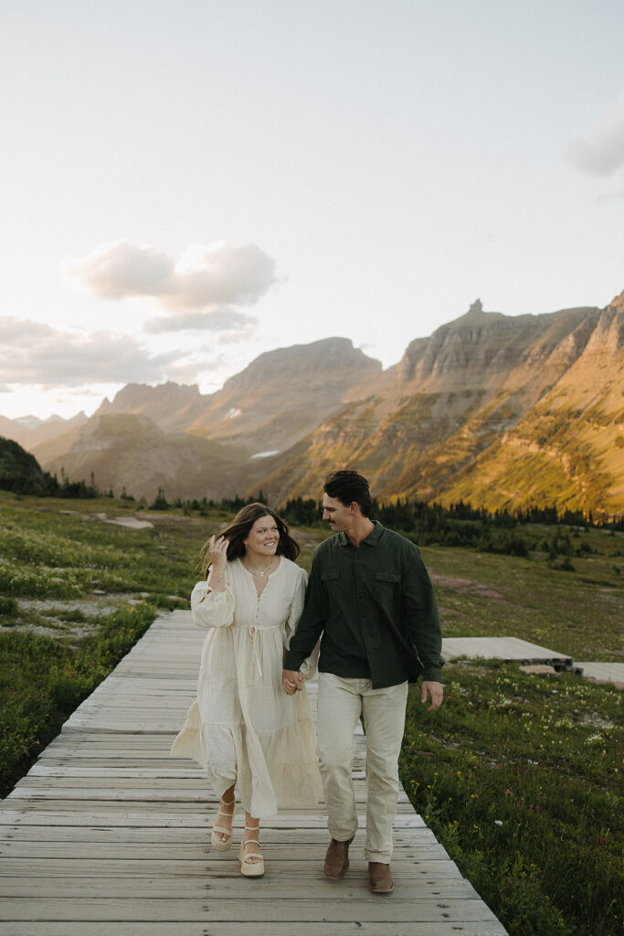 couple walks together at Glacier National Park sunset engagement