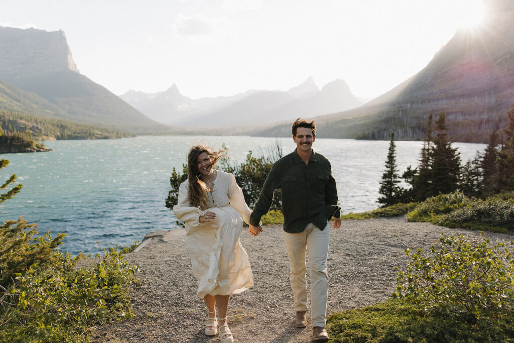 couple walks holding hands at windy Glacier National Park engagement
