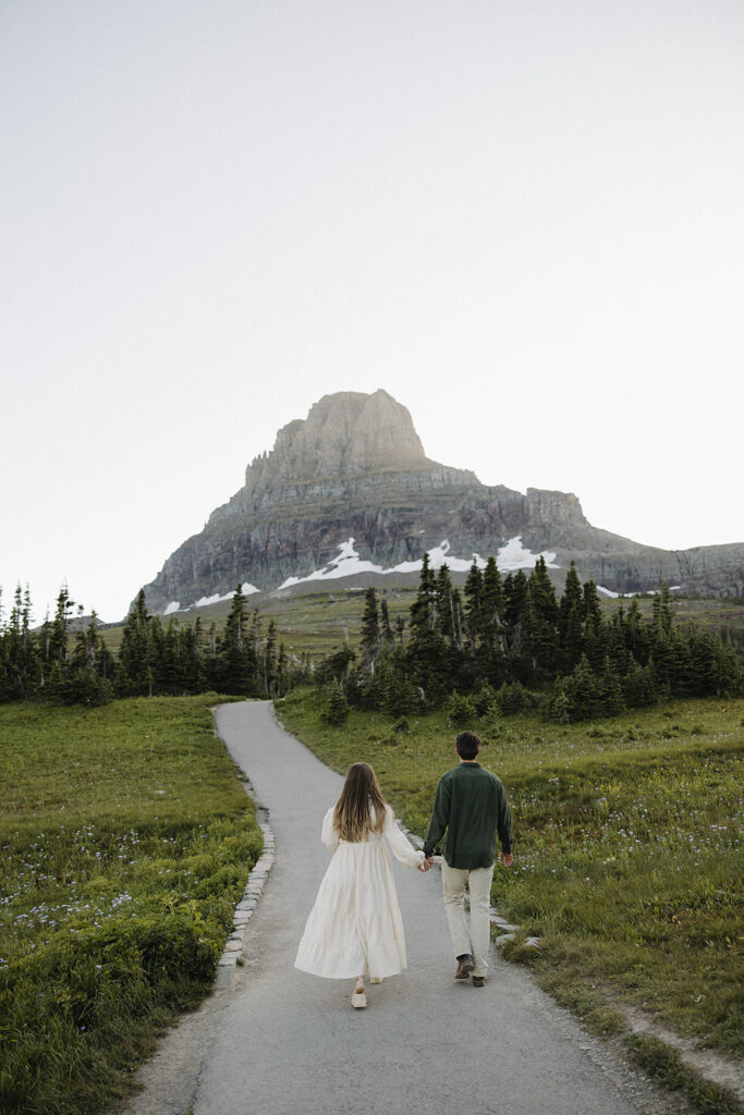 couple walks holding hands at windy Glacier National Park engagement
