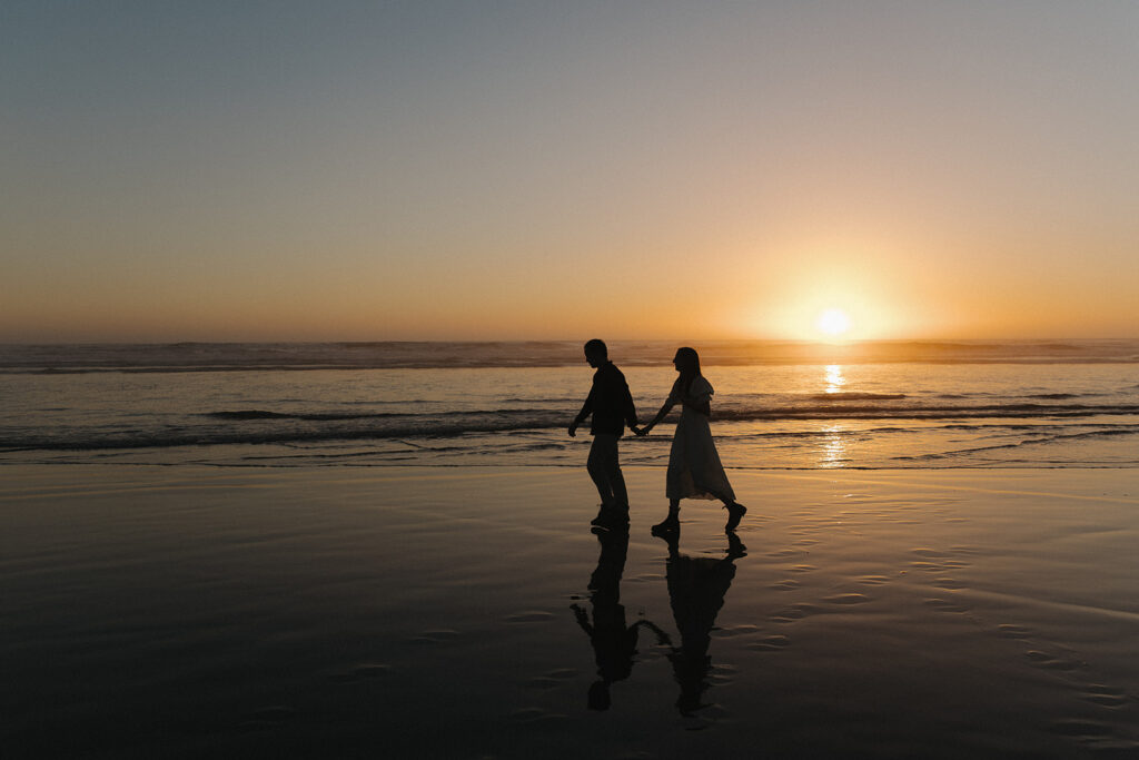 couple walks holding hands at Cannon Beach sunset engagement session