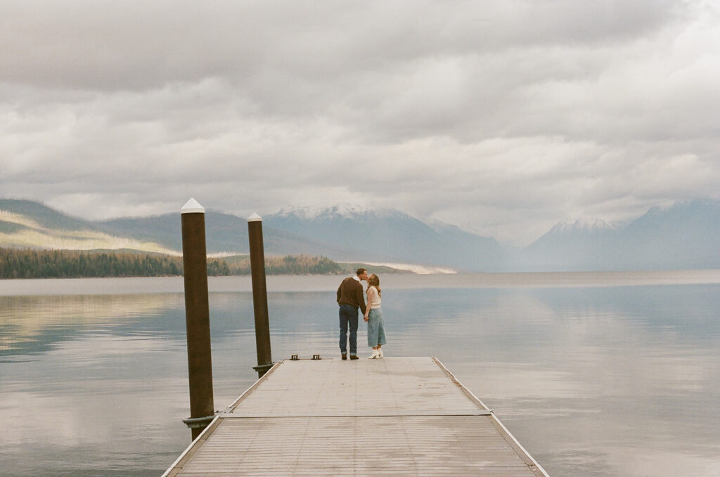 couple kisses on pier at Glacier National Park engagement