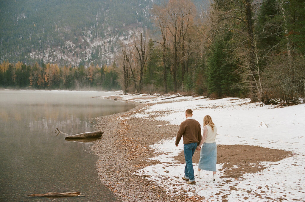 couple walks along snow-covered lake at Glacier National Park lake