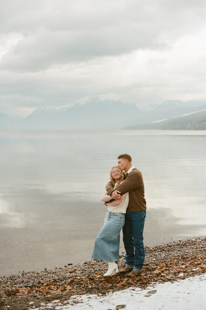 couple embraces along snow-covered lake at Glacier National Park lake