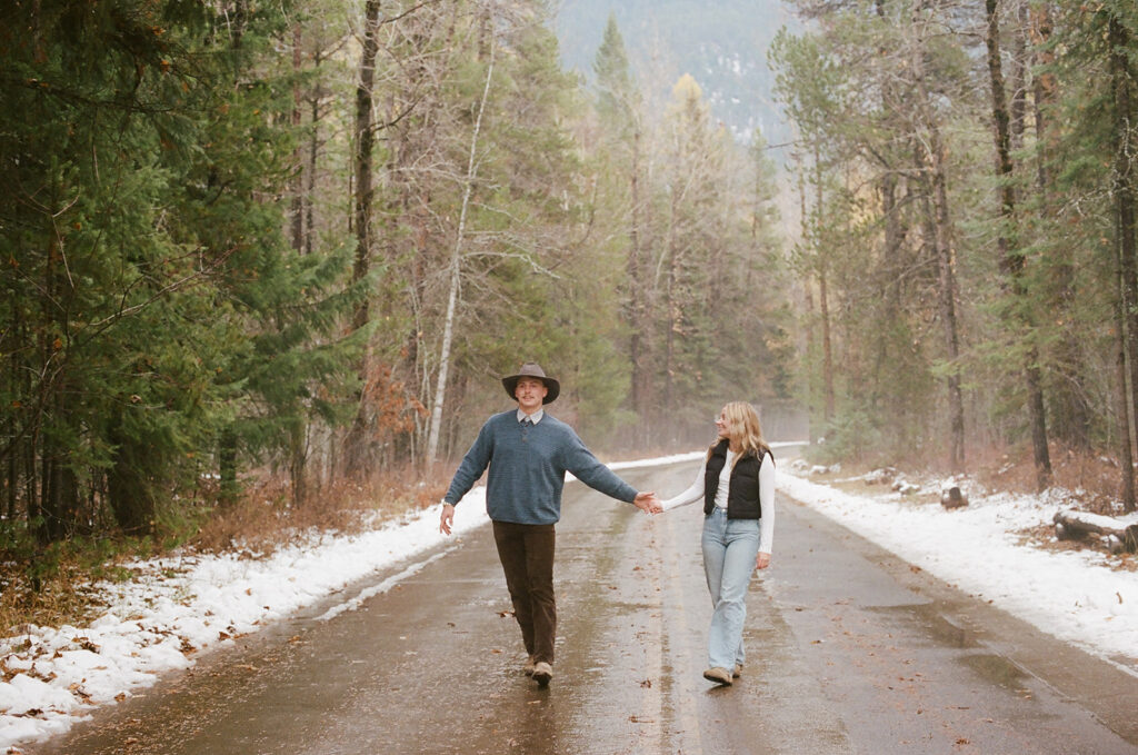 couple holds hands through woods at Glacier National Park engagement session 